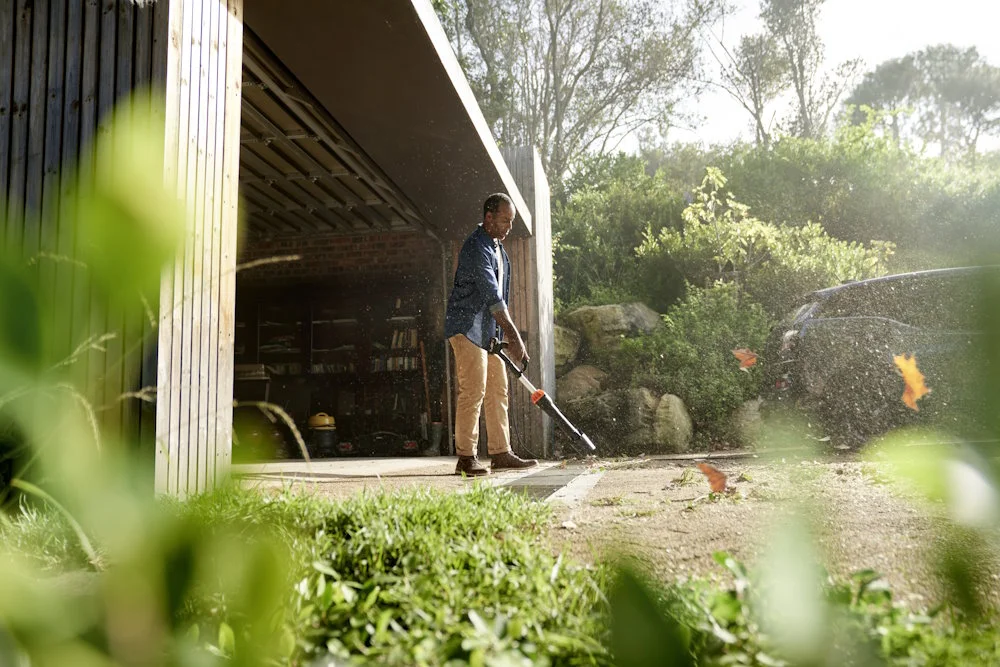 Person entfernt Laub mit Laubbläser.